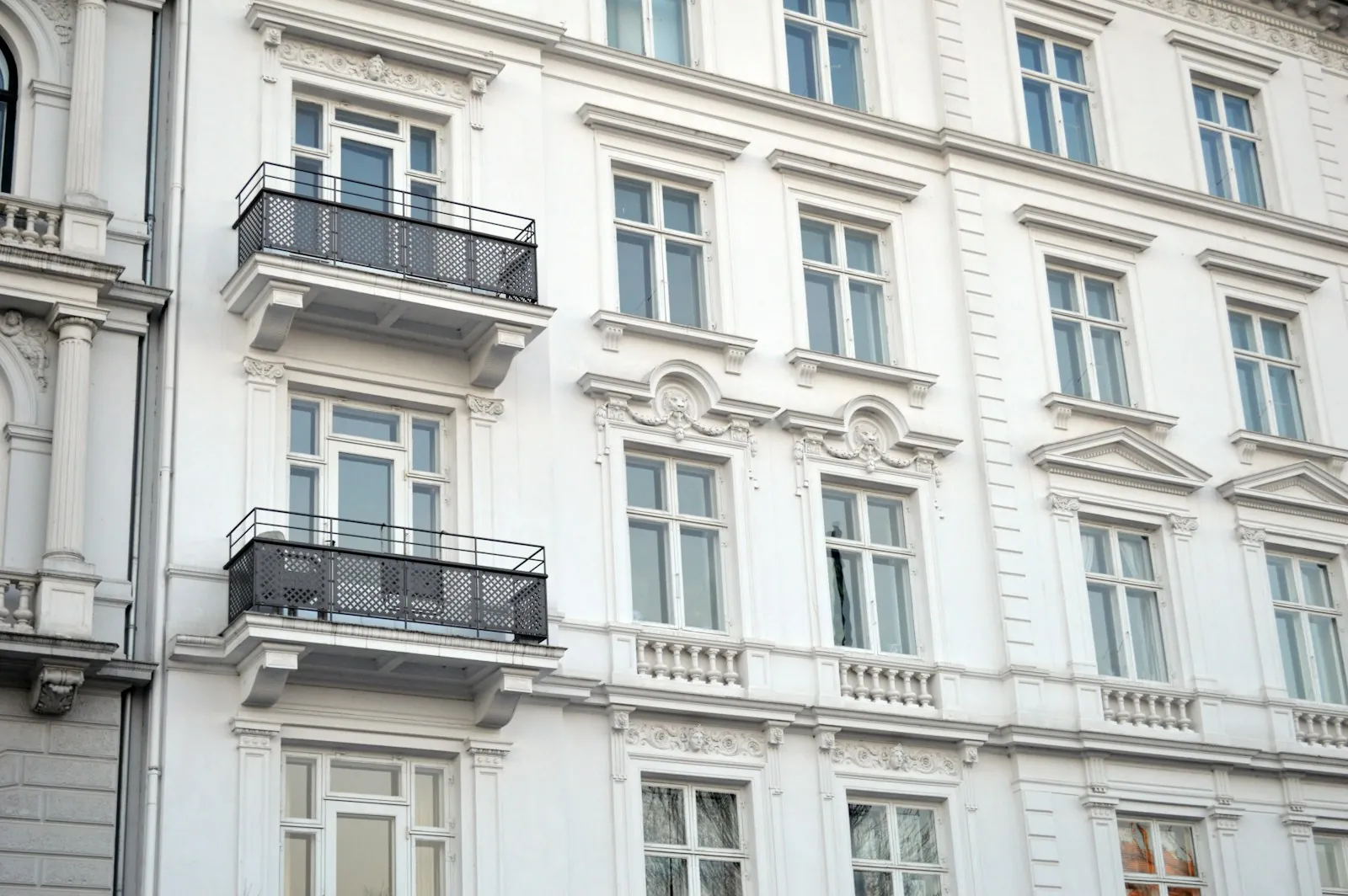 Fachada clásica blanca con balcones de forja y ventanas altas.